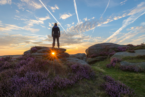 Picture of Mim, Jay's wife stood atop a rock with the sun shining through a gap below