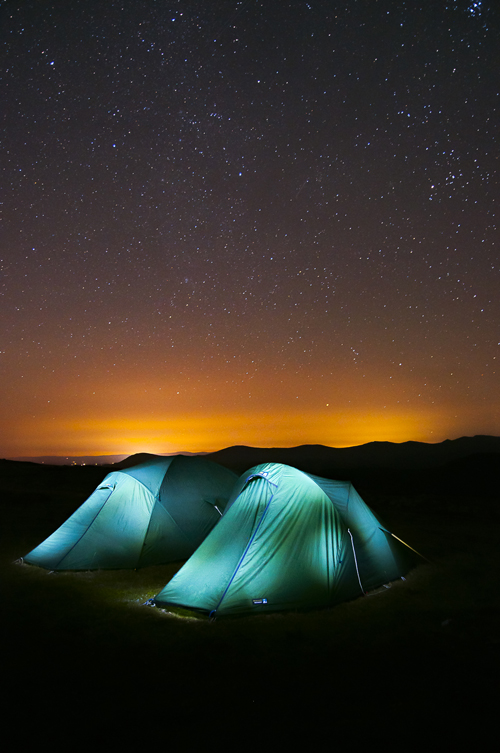 Image of two tents lit up in front of a clear night sky 